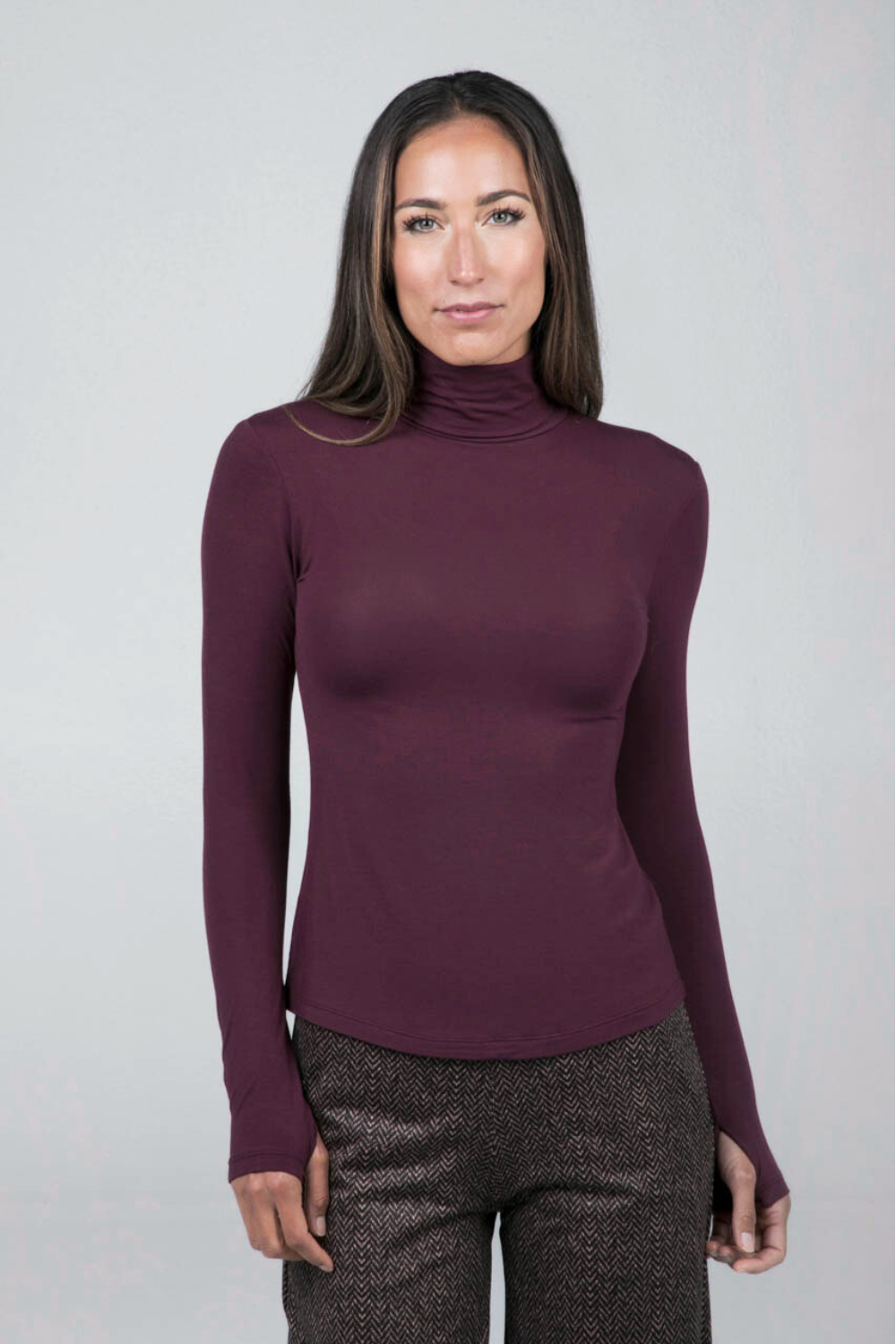 Woman wearing a burgundy turtleneck long sleeve top against a plain background