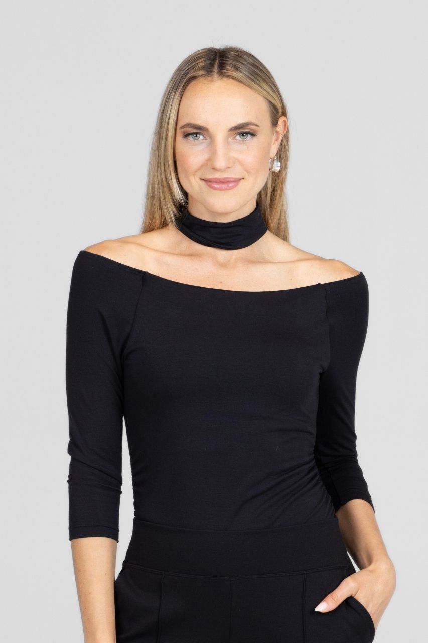 Woman wearing a black off-shoulder top with a mock neck collar against a gray background