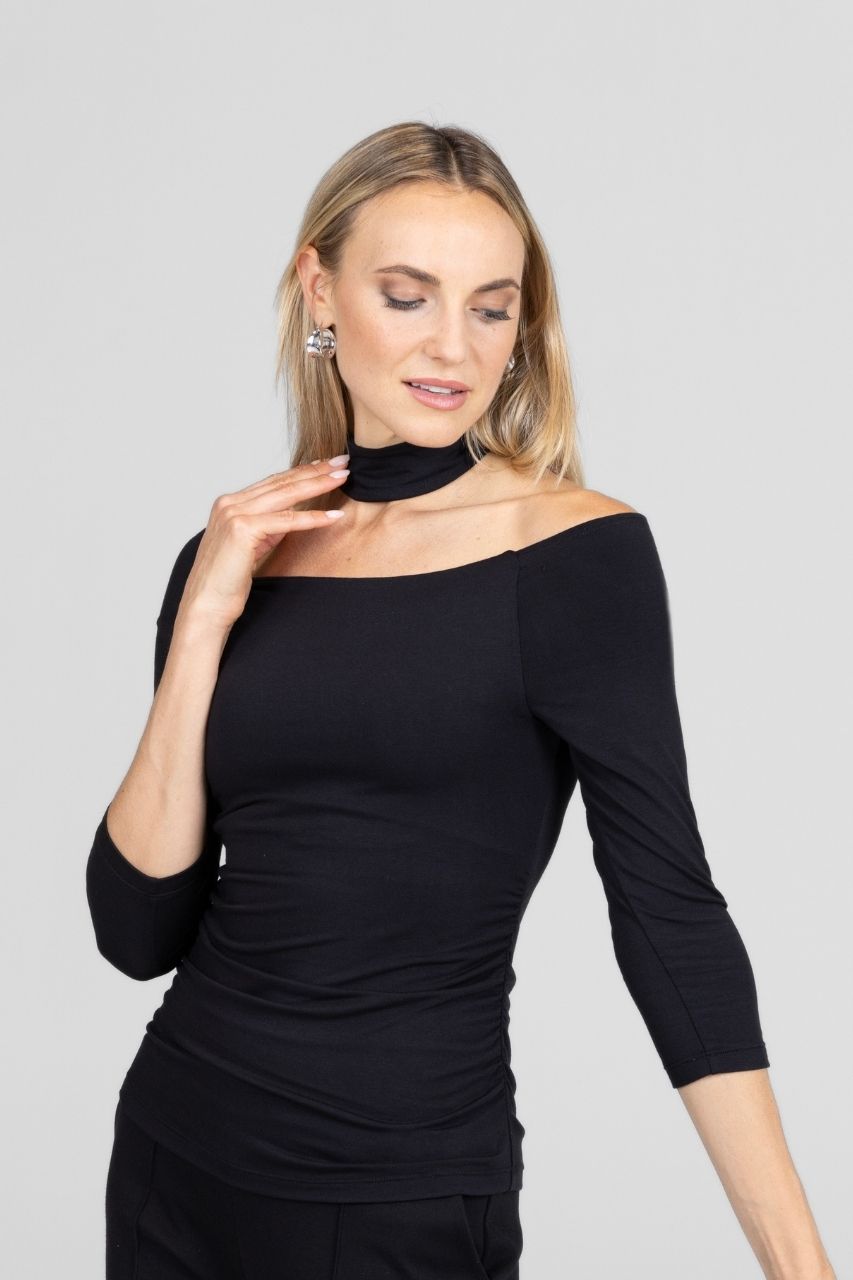 Woman wearing a black off-shoulder top with a mock neck against a gray background