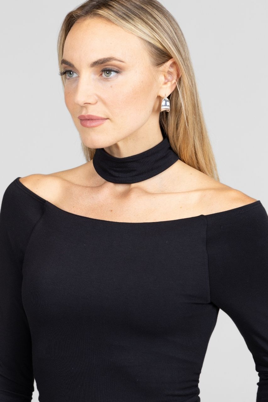 Woman wearing a black off-shoulder top with a mock choker against a gray background