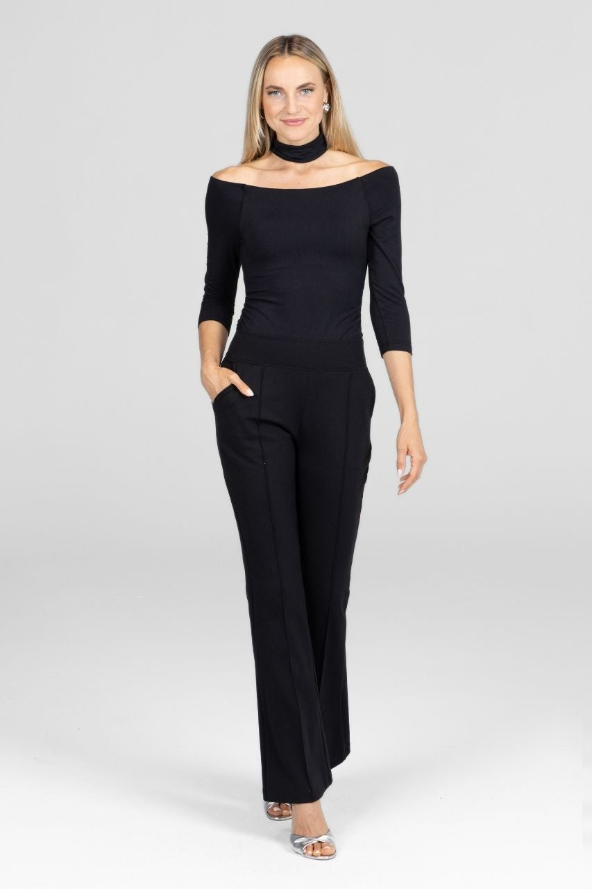 Woman wearing a black off-shoulder top with mock collar and black pintuck flared pants on a white background