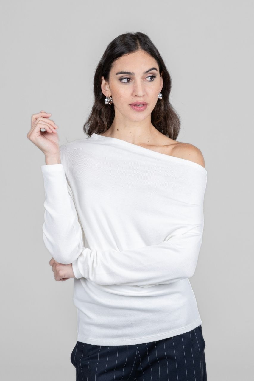 Woman wearing a white off-shoulder sweater against a gray background with pinstripe pants