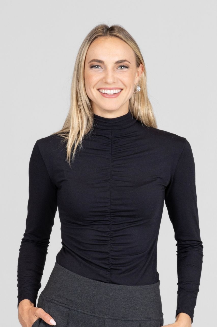 Woman wearing a black long-sleeve mock neck top tucked into charcoal high waisted pants against a plain background