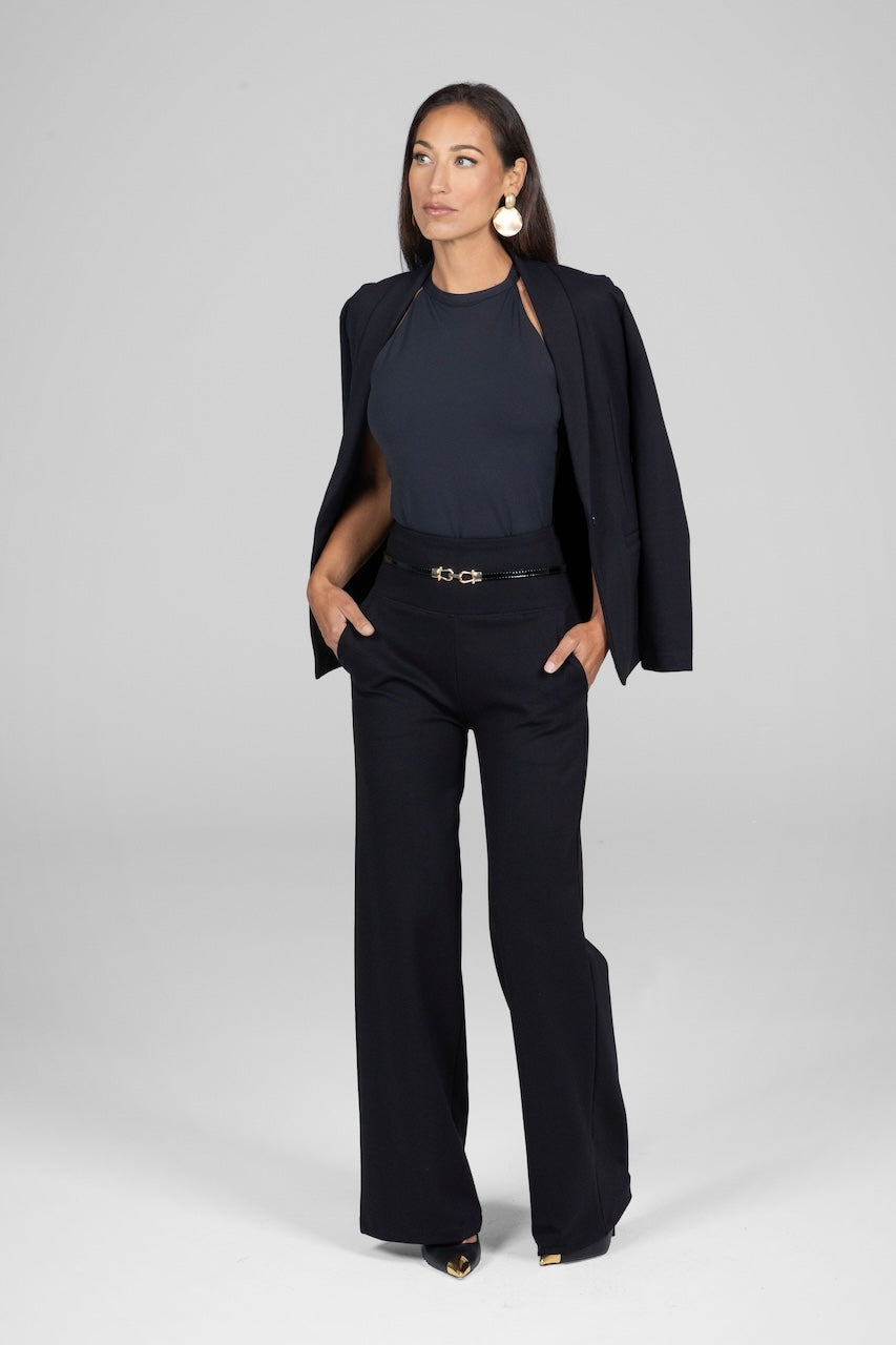 Full length photo of a woman wearing a black yoga halter top with black high waist wide leg pants and a black blazer over the shoulders.