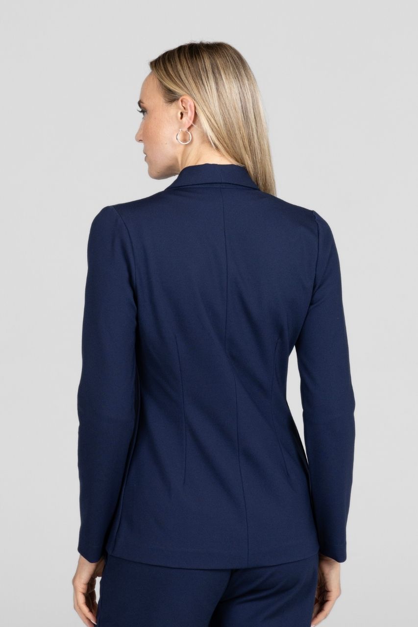 Back view of a woman wearing a navy blue blazer and matching pants on a light gray background