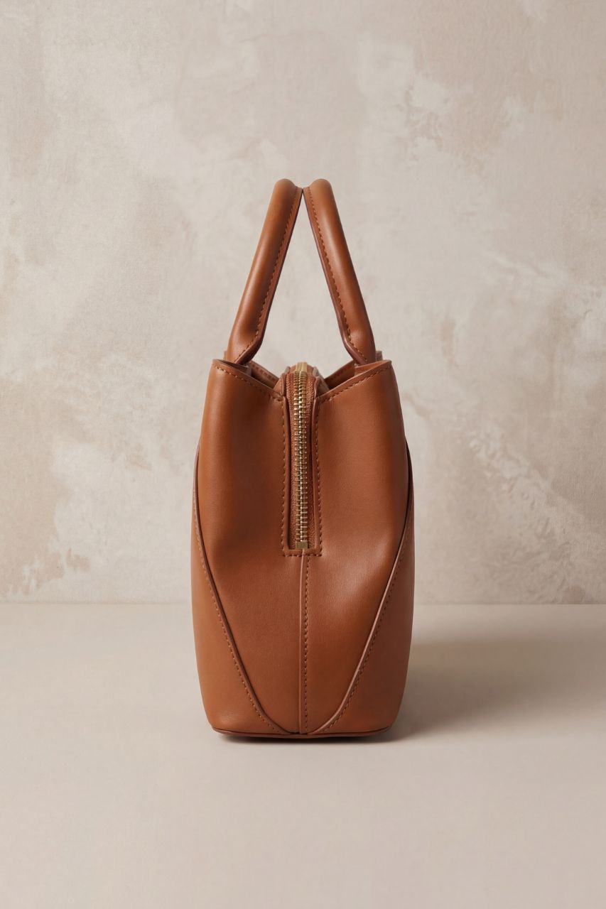 Side view of a brown PU leather handbag on a beige background