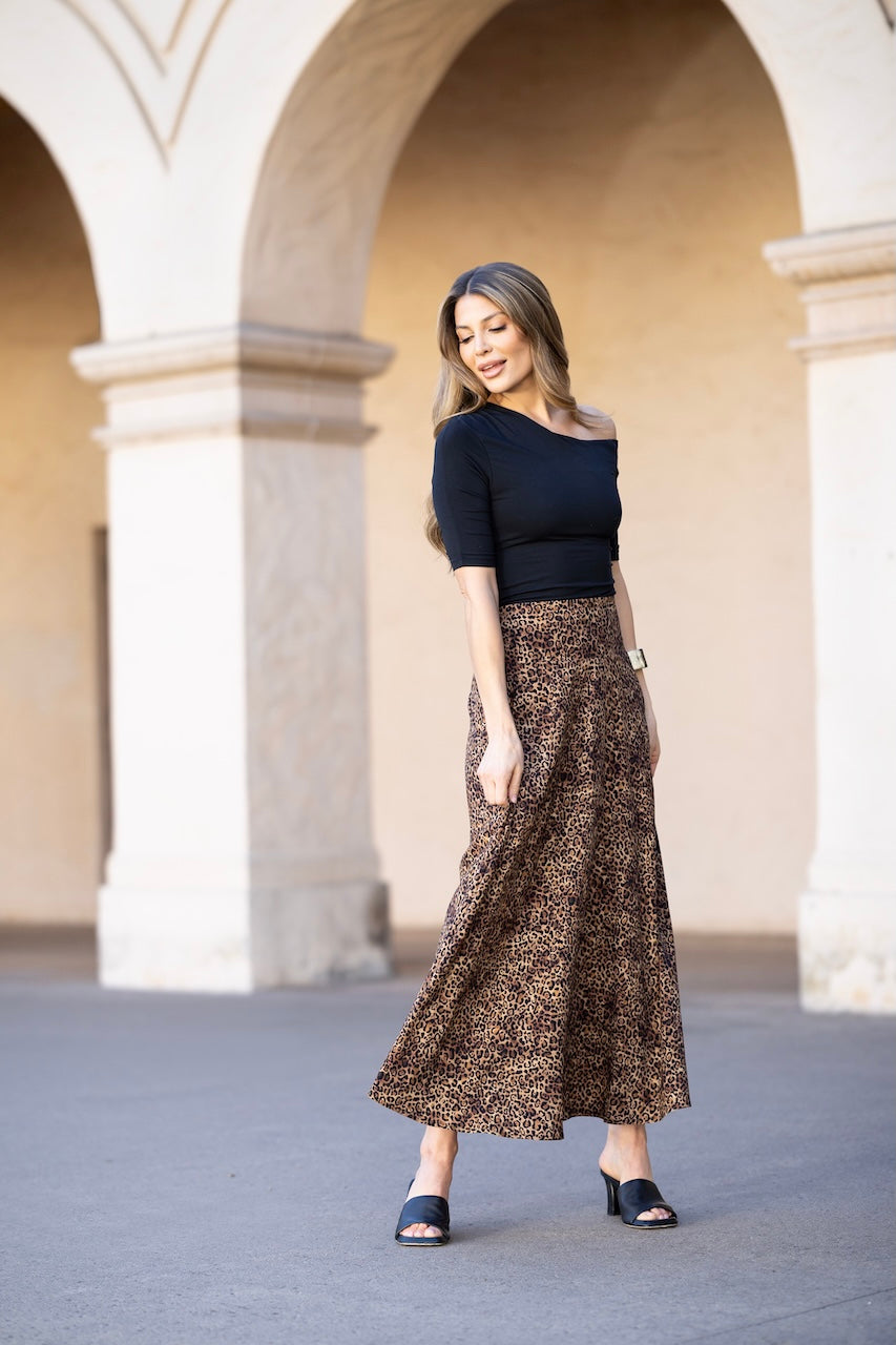 A woman wearing a animal patterned skirt and a solid color top standing in front of a columned background.