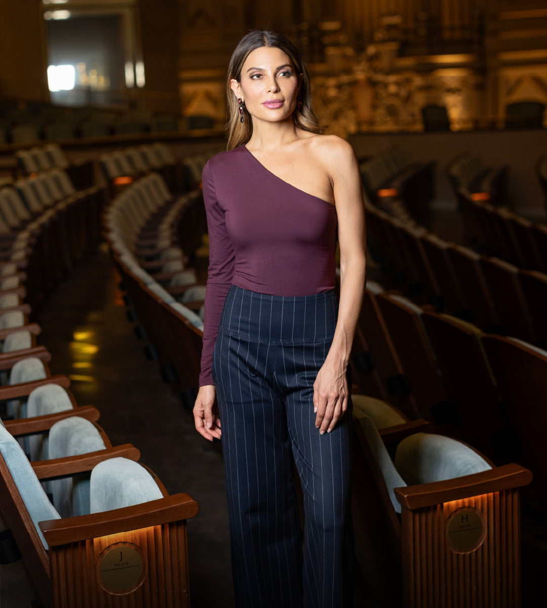 Woman in a burgundy one sleeve top and dark pinstripe pants standing in an empty theater.
