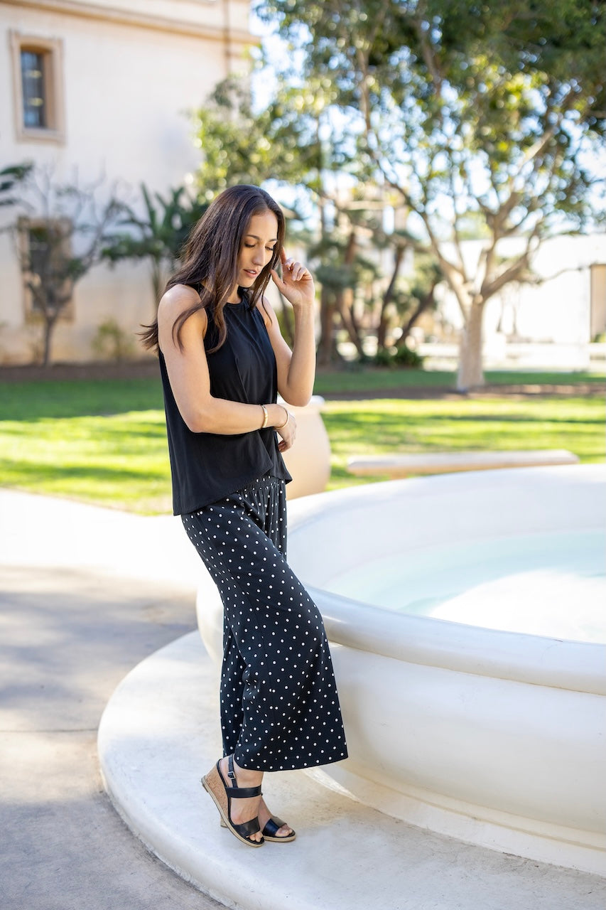 Woman in black sleeveless top and polka dot pants standing outdoors.