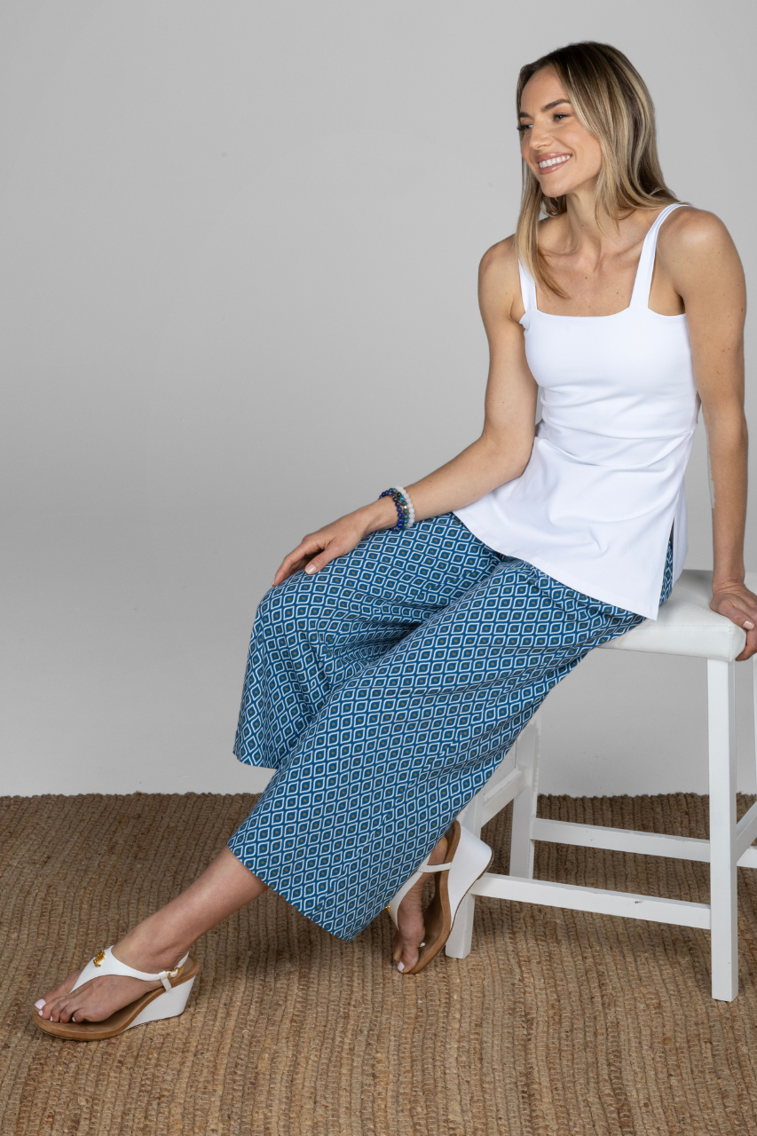 Woman sitting on a white stool wearing a white side slit cami and blue geometric patterned ankle pants