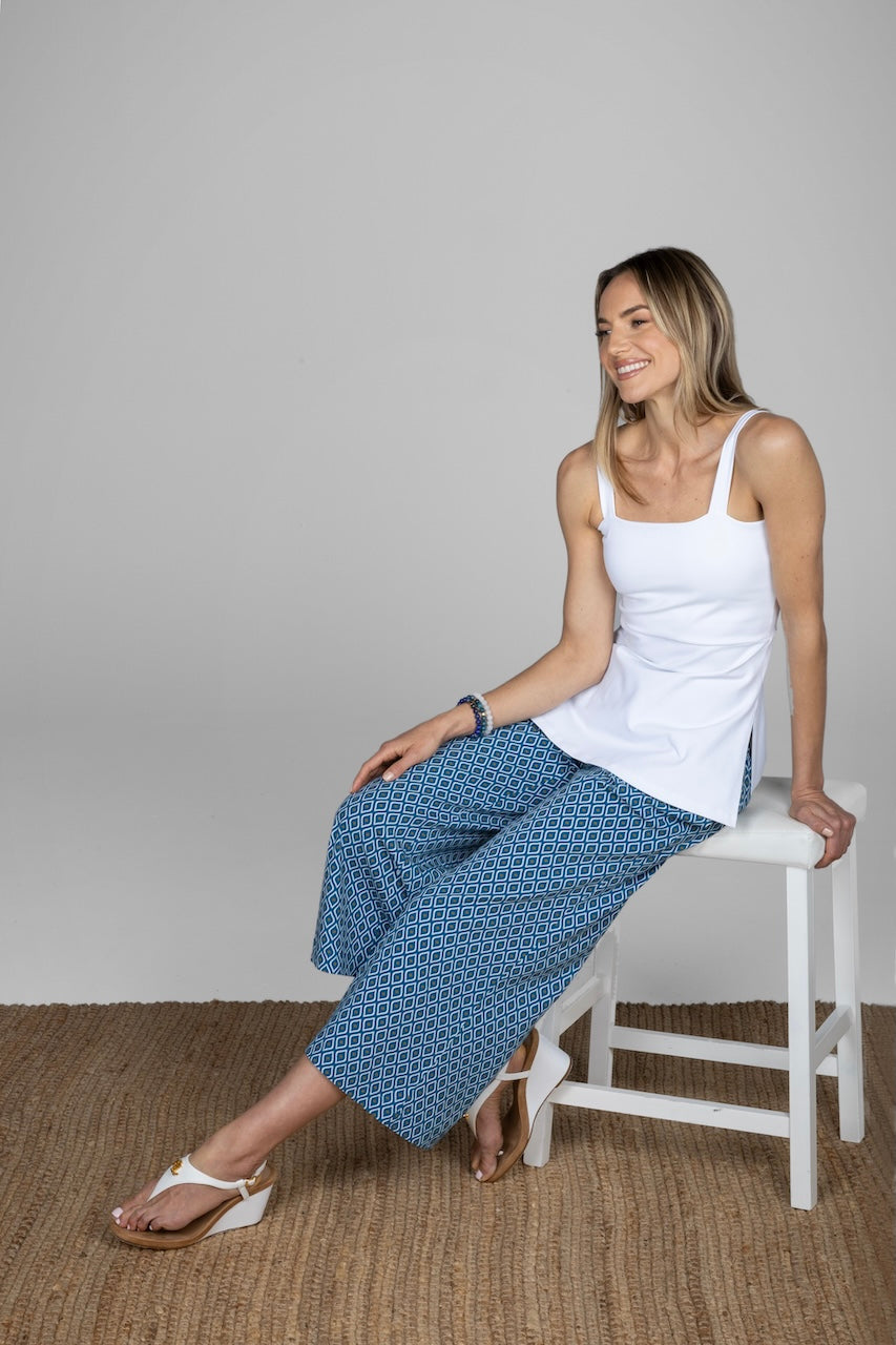 Woman sitting on stool and wearing a white sleeveless cami with blue ankle pants with a geometric print