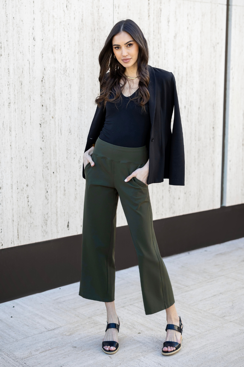 Woman wearing blazer over her shoulders wearing a black v-neck tank and green ankle pants