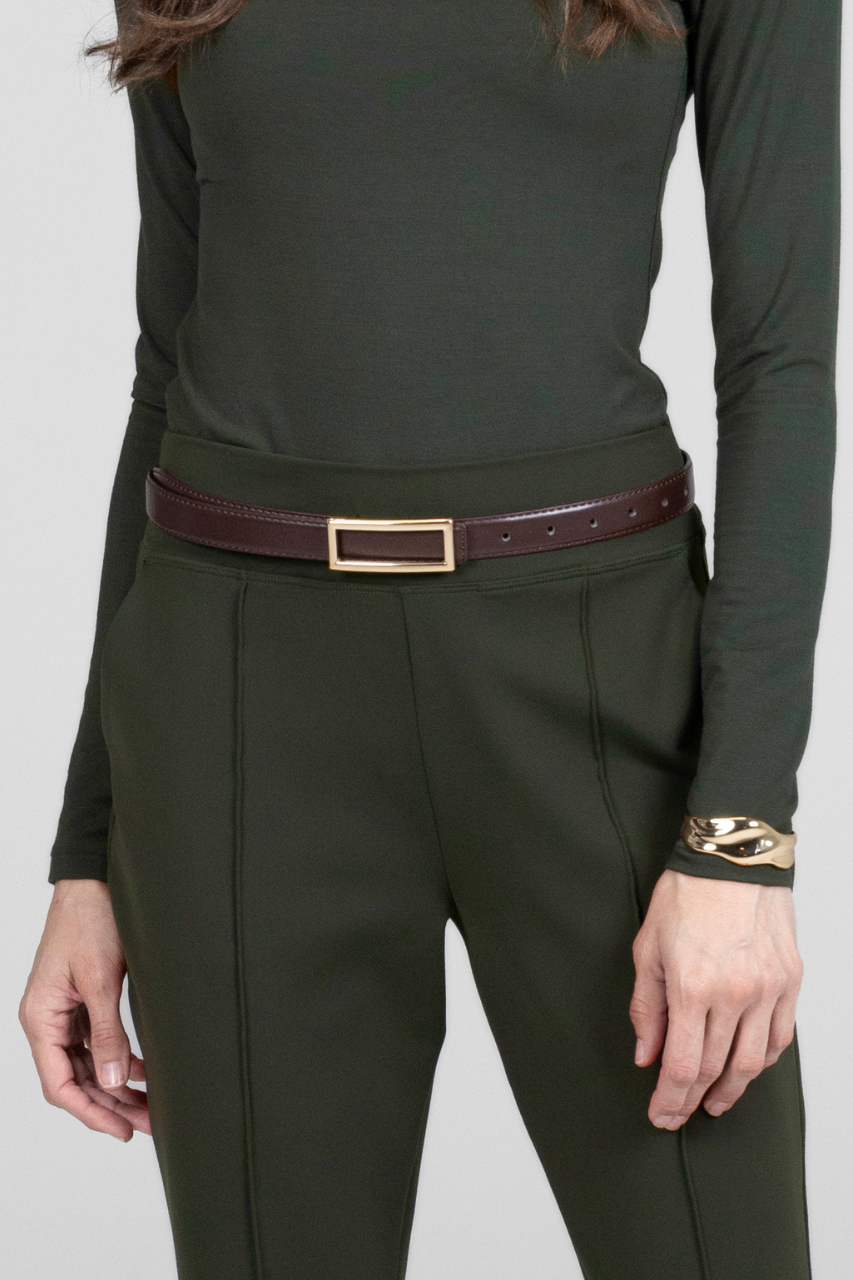 Person wearing a green long-sleeve top and dark green pants with a dark brown belt and gold bracelet on a light gray background