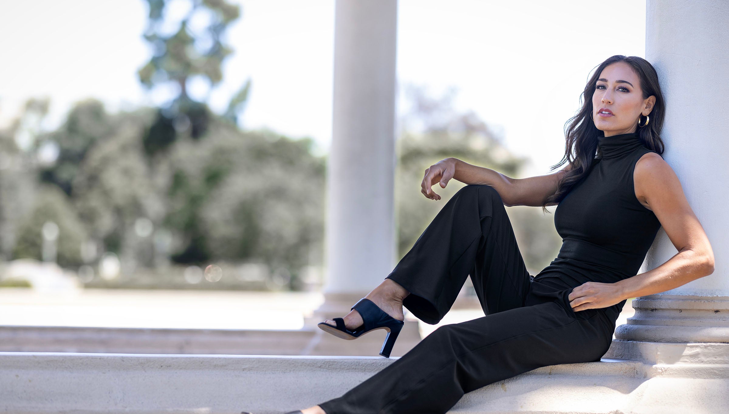 Woman leaning back on a pillar wearing black yoga pants with a mock neck top