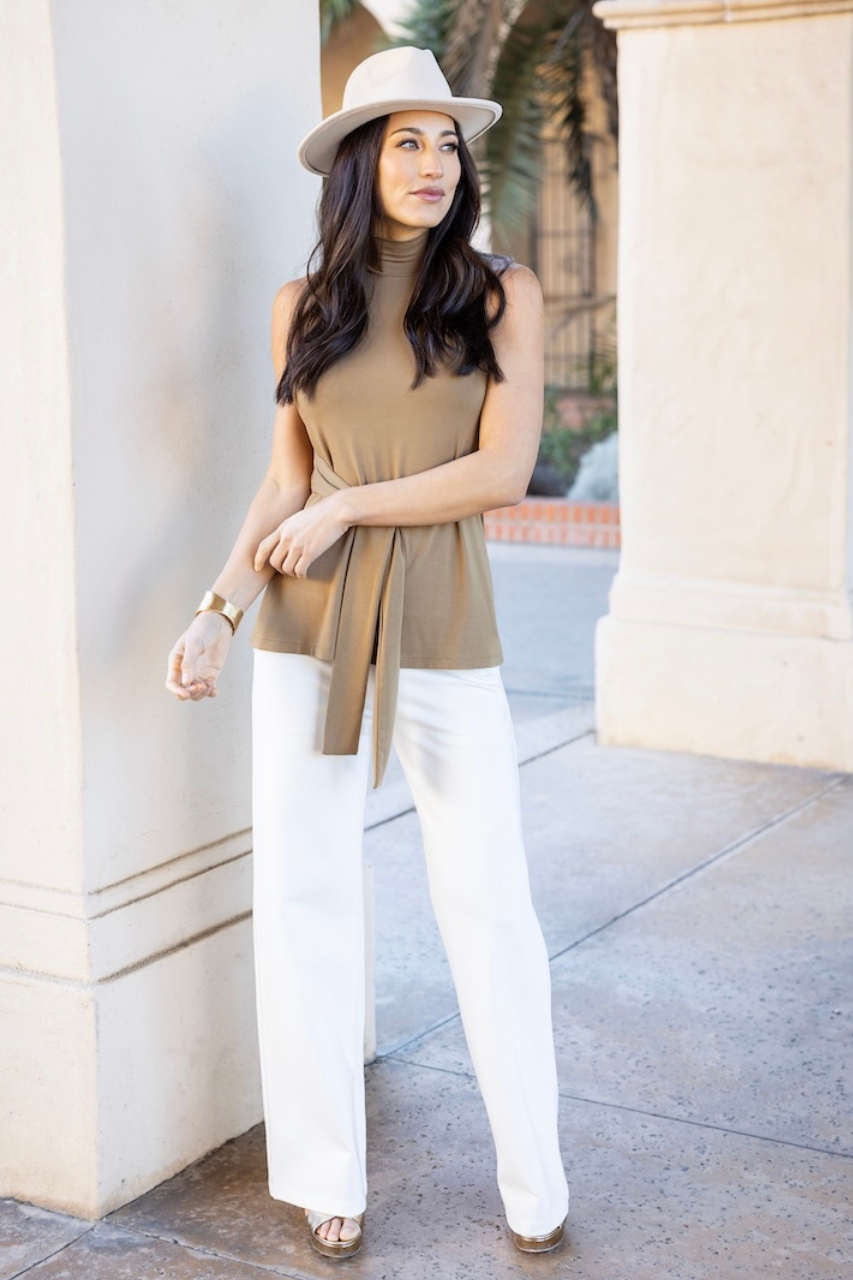 Woman wearing a beige hat with beige mock neck tunic with waist tie and white high waist wide leg pant