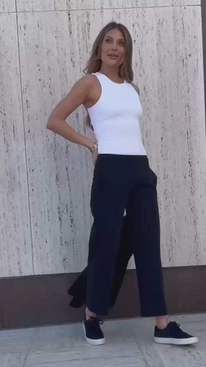 Video of woman posing wearing a white tank top and black ankle pants