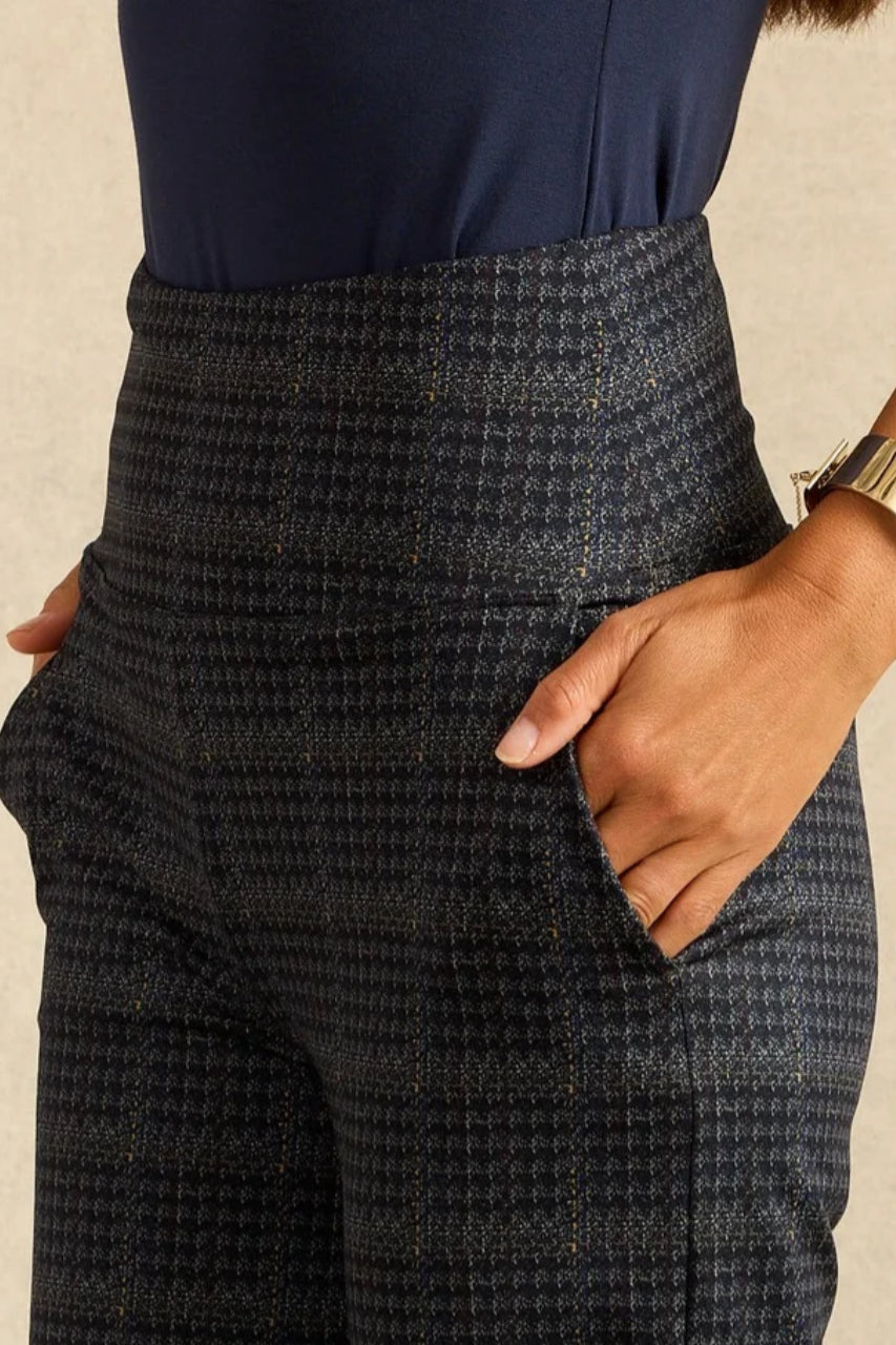 Close-up of a person wearing dark navy and gray micro-houndstooth trousers with a hand in the pocket, paired with a navy top.