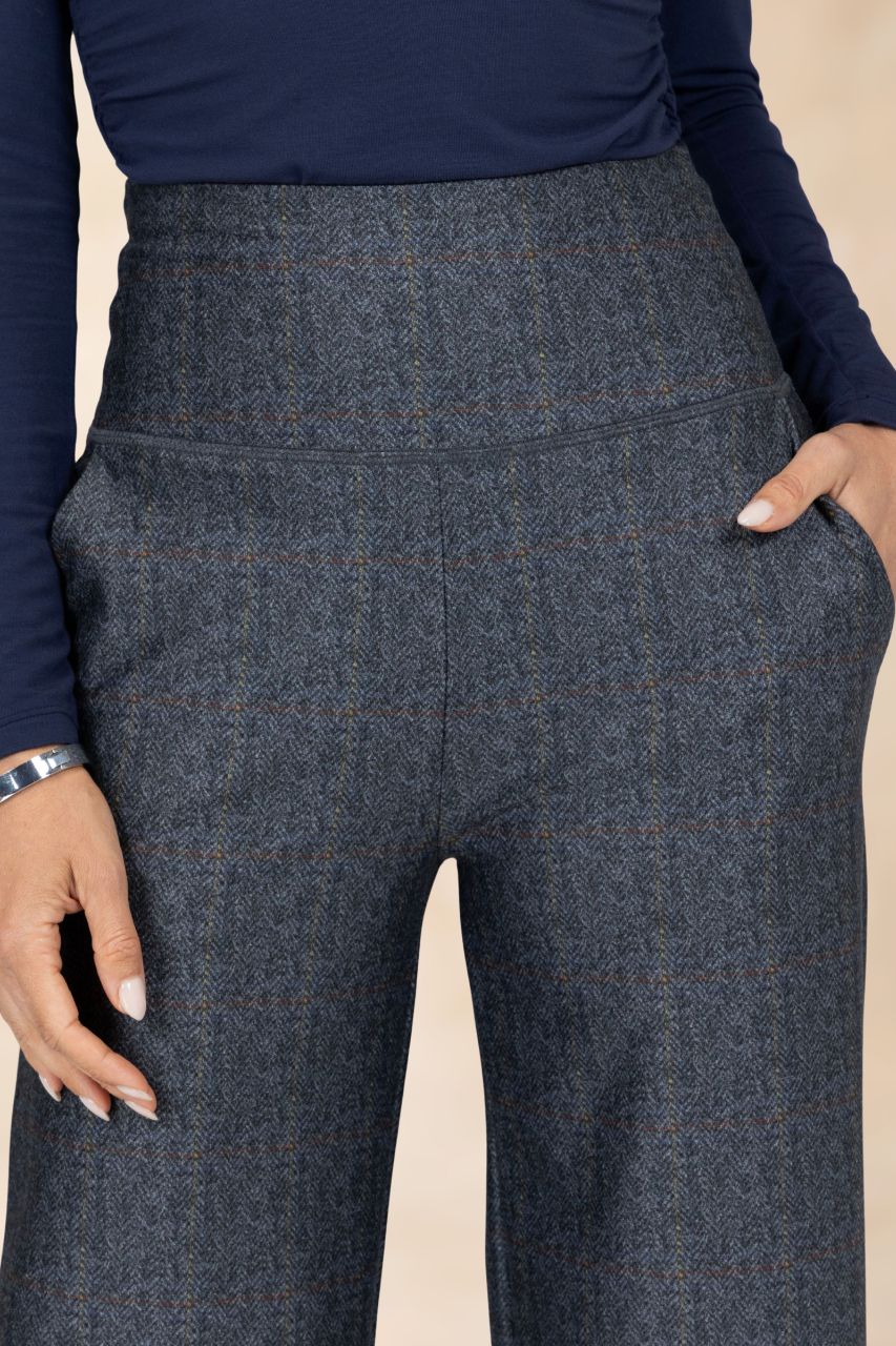 Grey tartan patterned pants worn with a navy long-sleeve top on a beige background