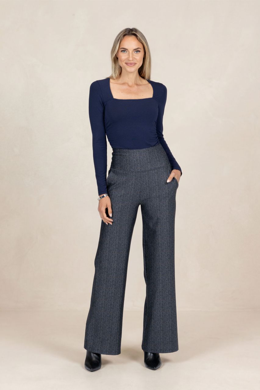 Woman wearing a navy top and gray tartan pants on a beige background