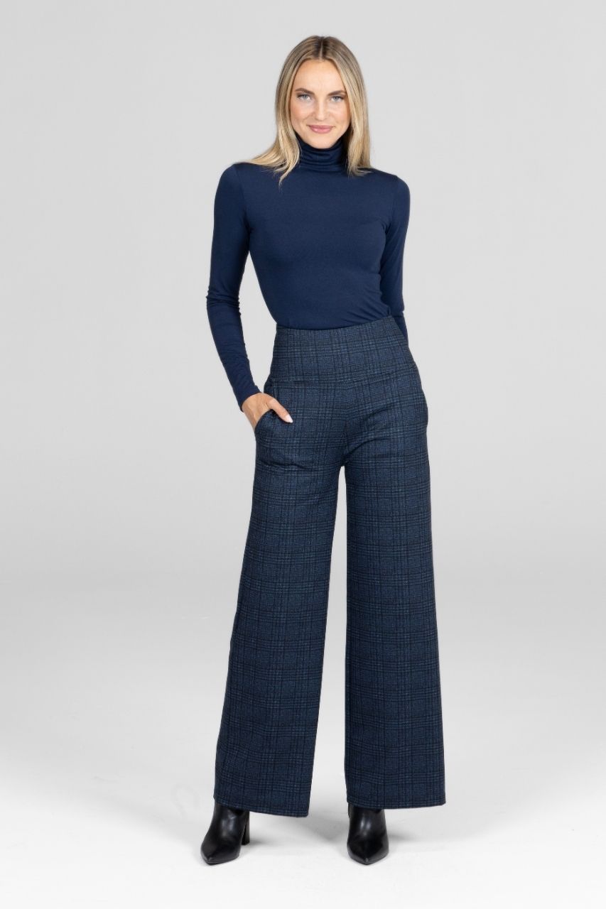 Woman wearing a navy turtleneck and plaid high waist wide leg pants on a white background
