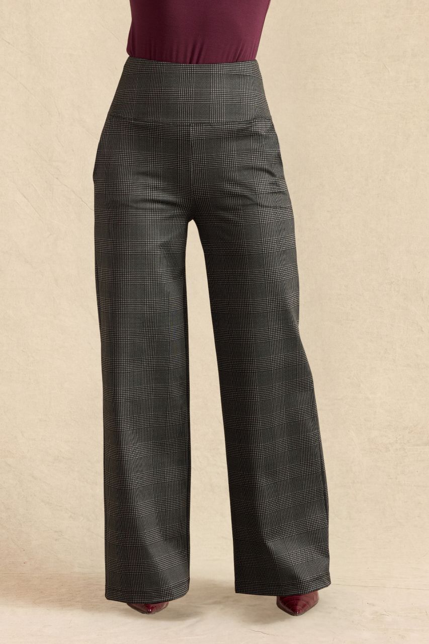 A pair of dark gray wide-leg plaid trousers shown on a model from the waist down, paired with a burgundy top and burgundy shoes, against a textured beige background.