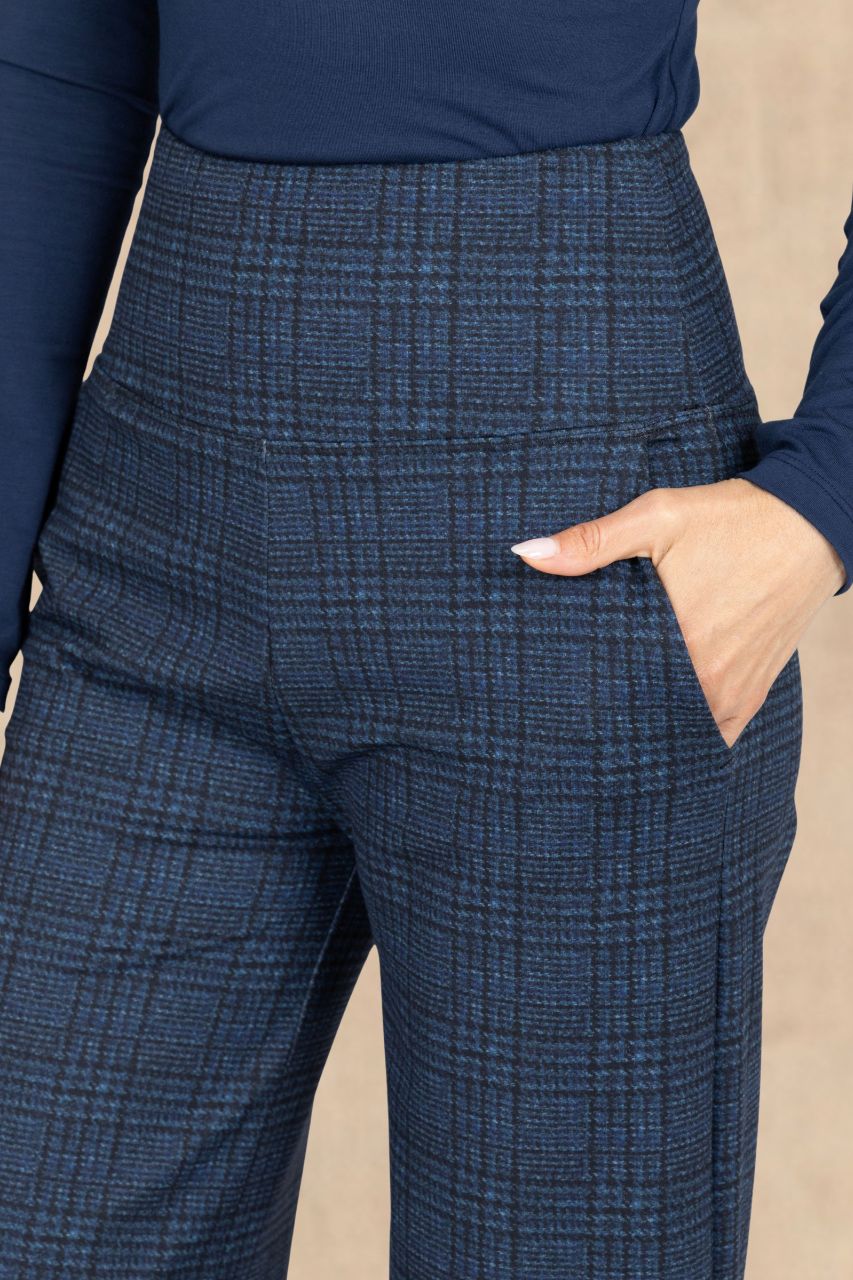 Close-up of a person wearing high-waisted navy plaid trousers with a side pocket, paired with a navy long-sleeve top against a neutral beige background.