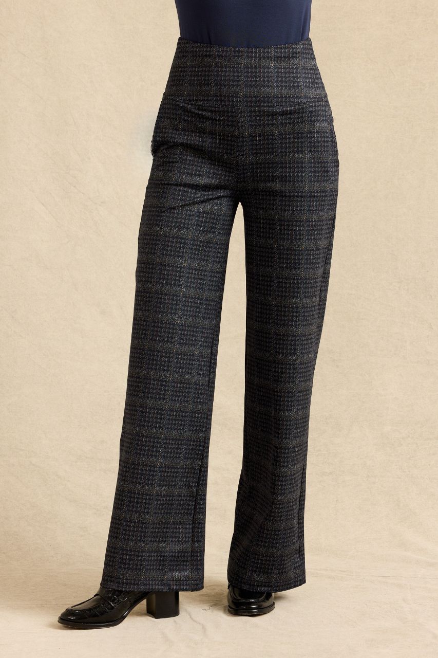 A person wearing dark charcoal plaid wide-leg trousers, standing against a beige textured backdrop.