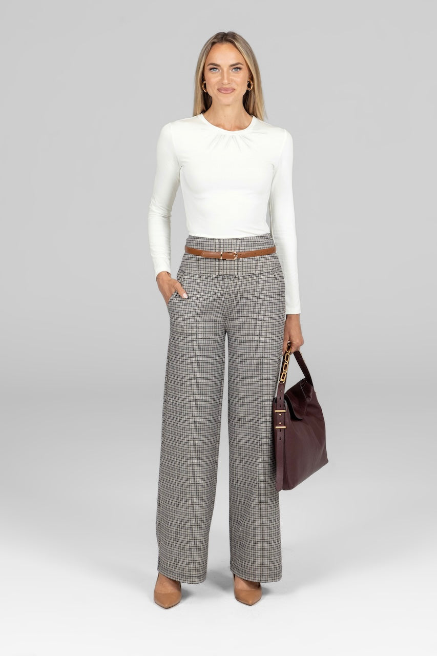A woman wearing a white long sleeve top and gray wide-leg high-waisted pants with a checkered pattern. 