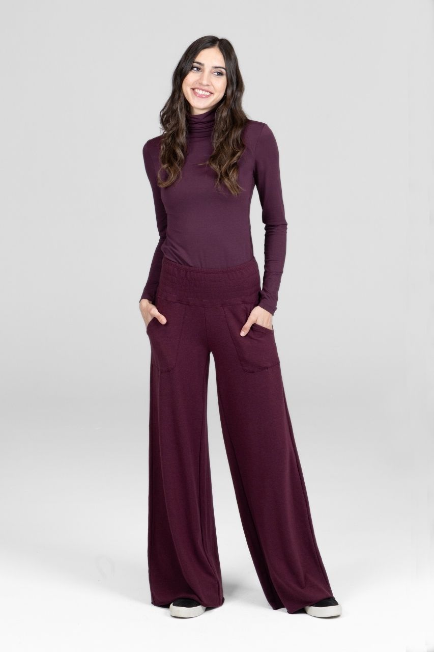 Woman wearing a burgundy outfit with a turtleneck and wide-leg pants on a white background