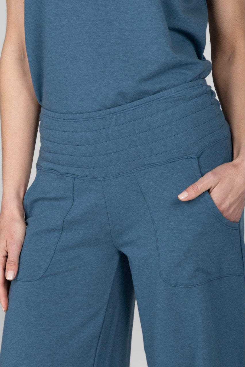 A close-up of a woman wearing a blue crop yoga pant with a wide leg and an elastic waistband.