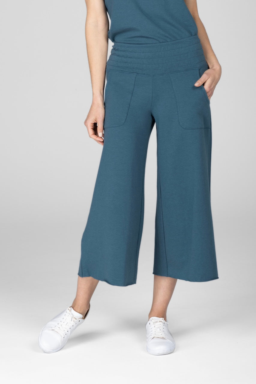Front view of a woman wearing blue cropped yoga pants and white sneakers with one hand in front pocket