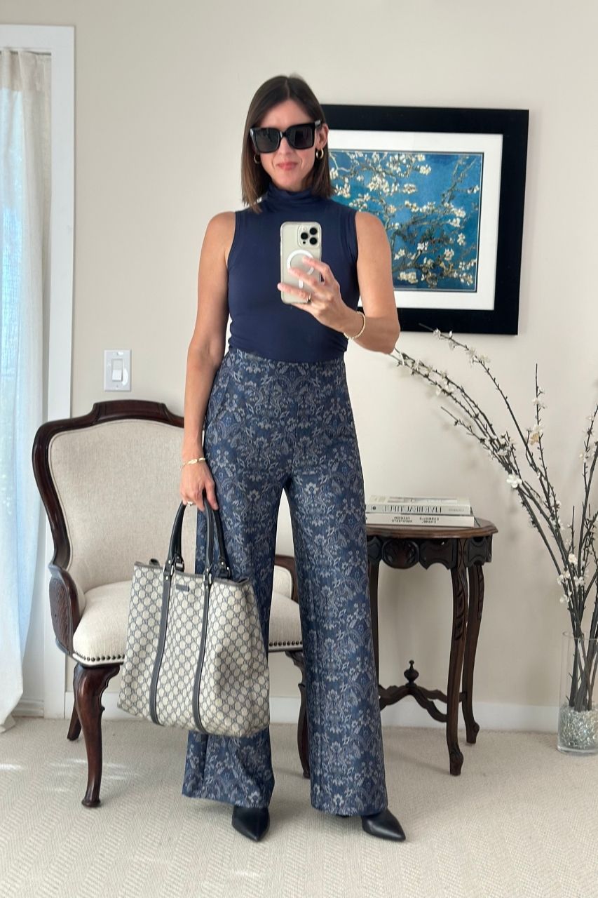 Woman taking a mirror selfie wearing a navy sleeveless top and navy medallion wide leg pants, holding a handbag.