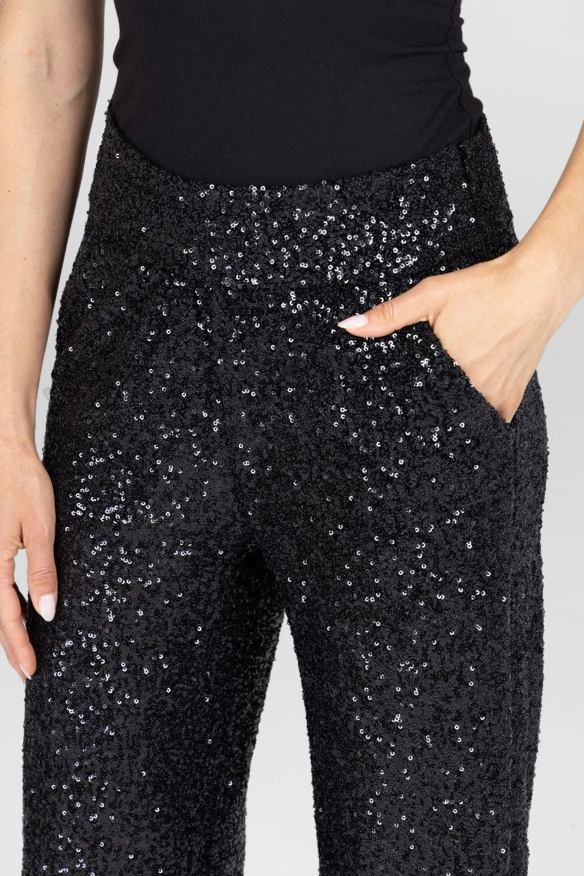 Close up view of a black sequin pants worn by a woman on a light gray background