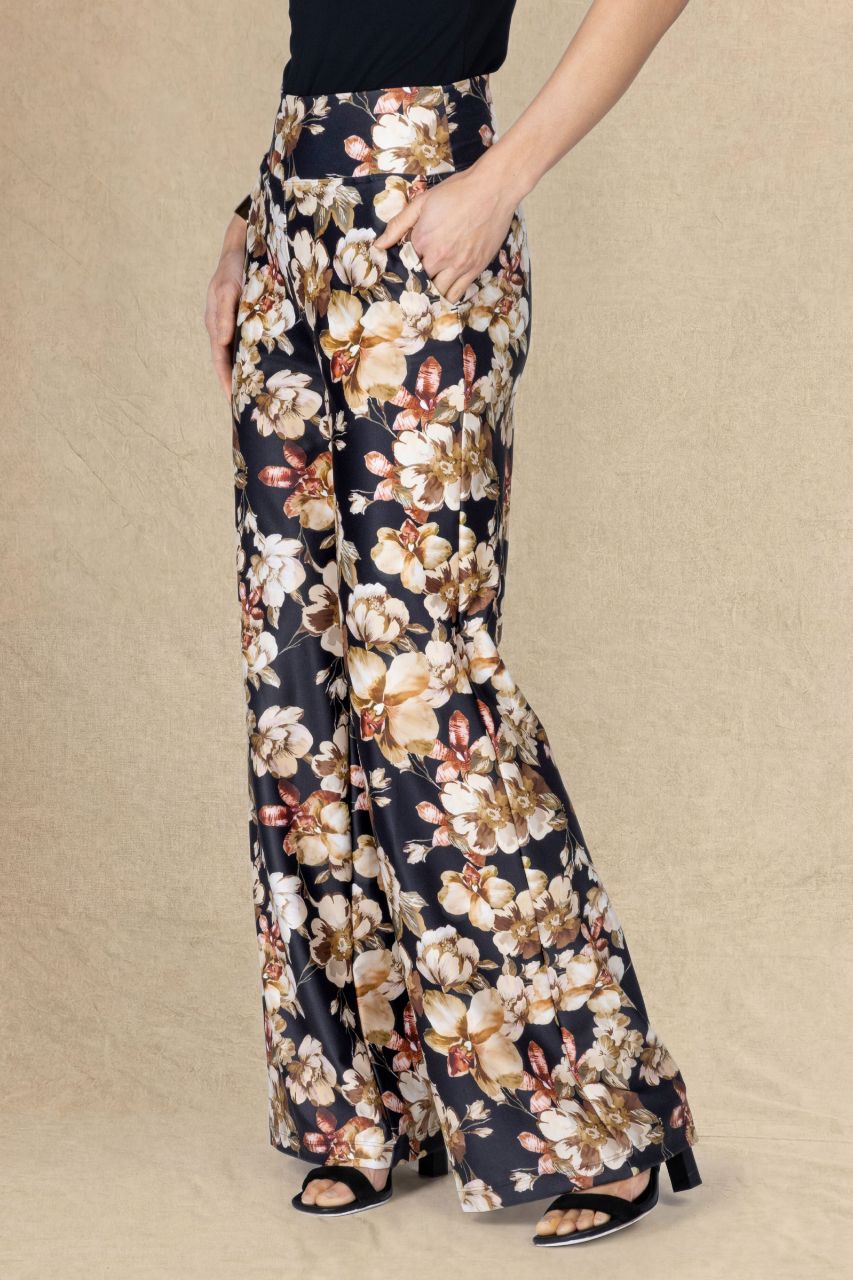 Side view of a woman wearing fall floral high rise wide leg pants on a beige backgbround