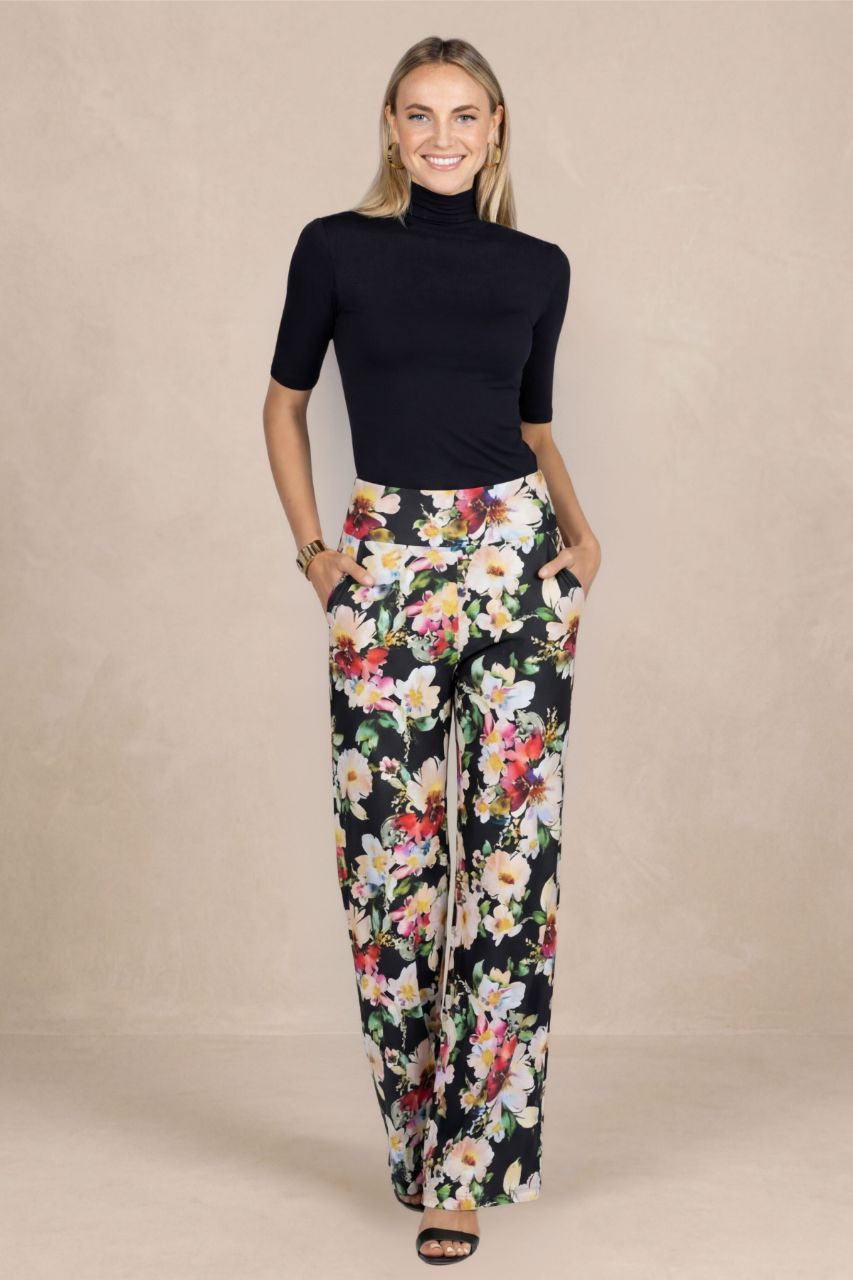 Woman wearing a black short sleeve mock neck and floral pants on a beige background