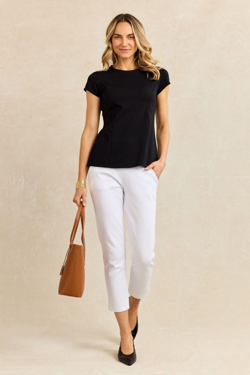 Woman wearing a black t-shirt and white pants, holding a brown handbag on a beige background