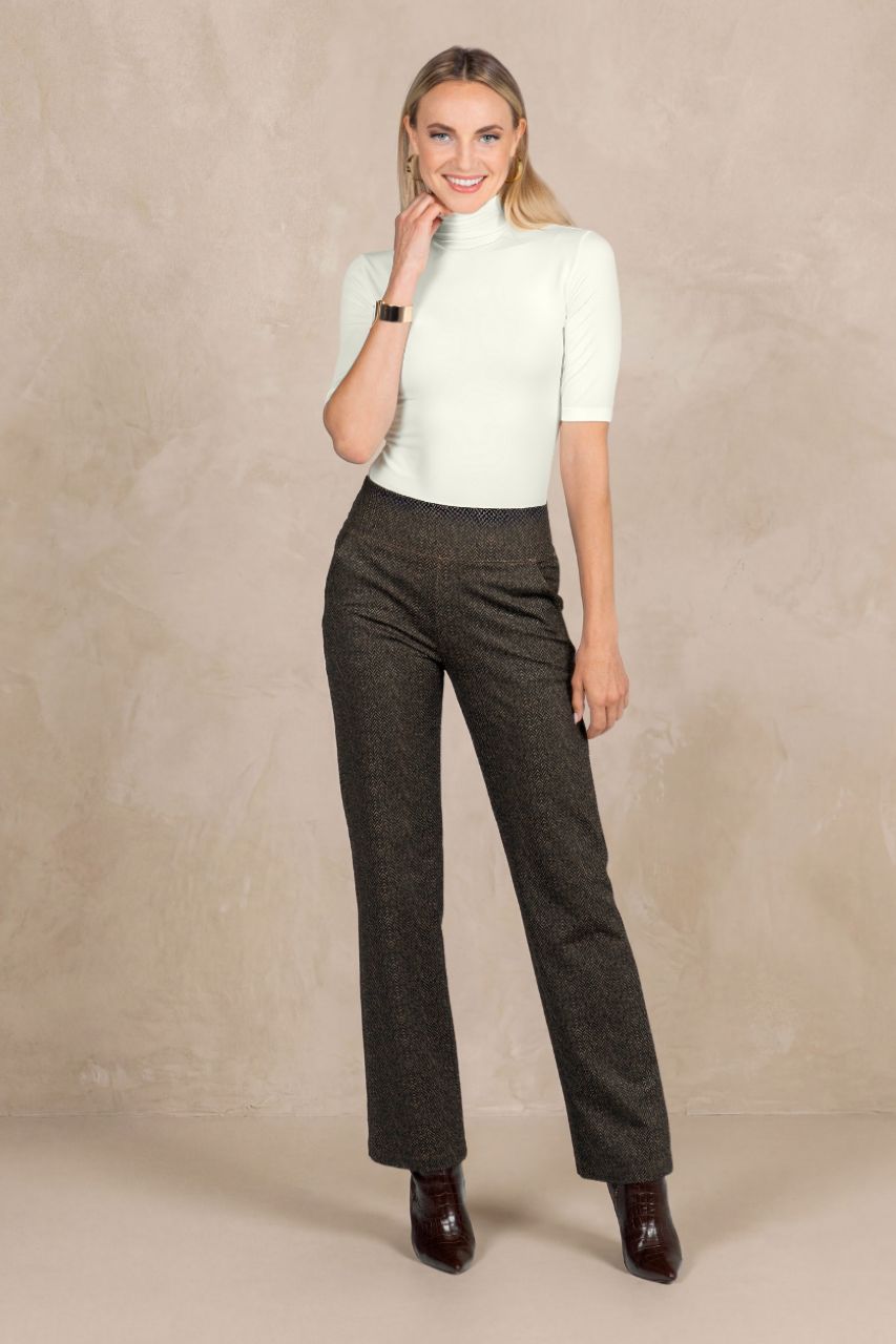 Woman wearing an ivory mockneck top and brown pants against a beige background