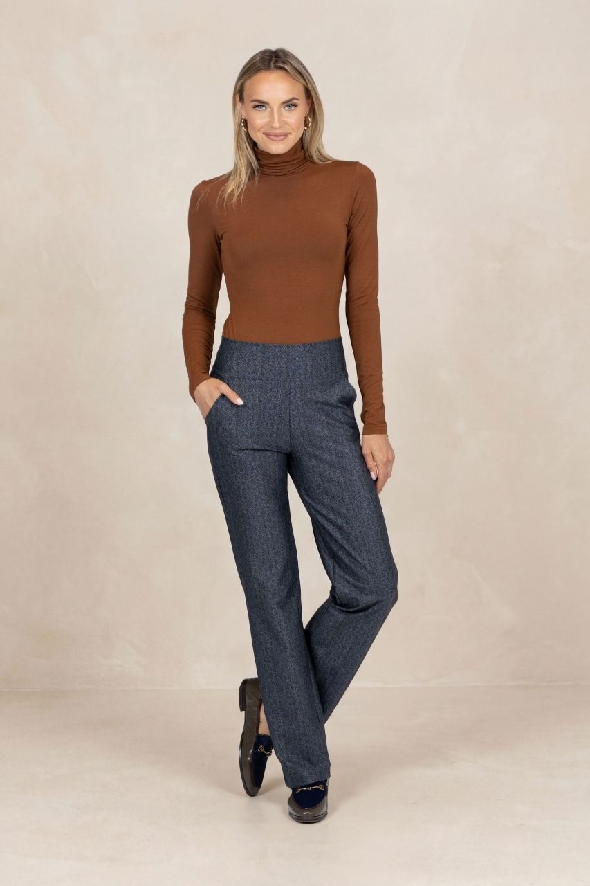 Woman wearing a brown turtleneck and tartan straight leg pants on a beige background