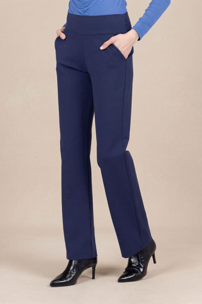 Woman wearing navy blue straight leg pants in front of a beige background 