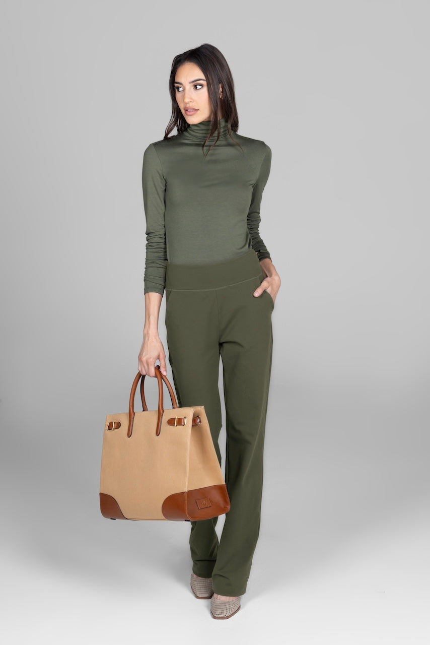 Woman in green turtleneck and pants holding a tan handbag.