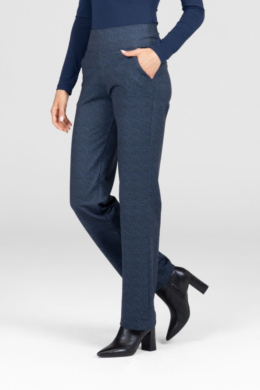 Woman wearing a navy top and blue straight leg pants with black shoes on a white background