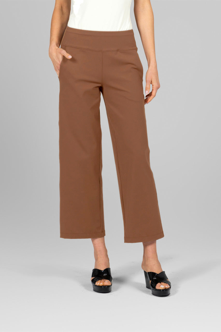 Woman modeling dark khaki ankle pants with hands in pockets, paired with an ivory turtleneck and black platform sandals.