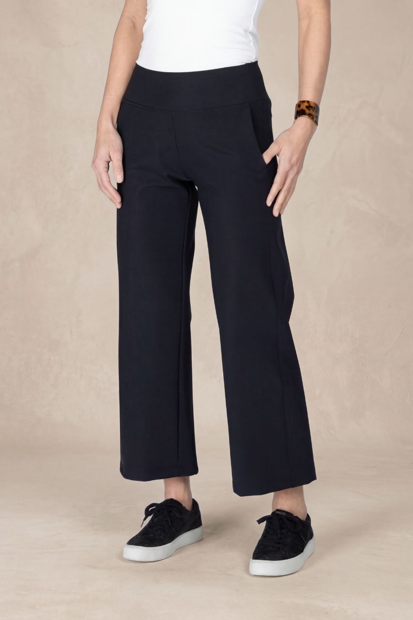 Person wearing black ankle pants and sneakers on a beige background