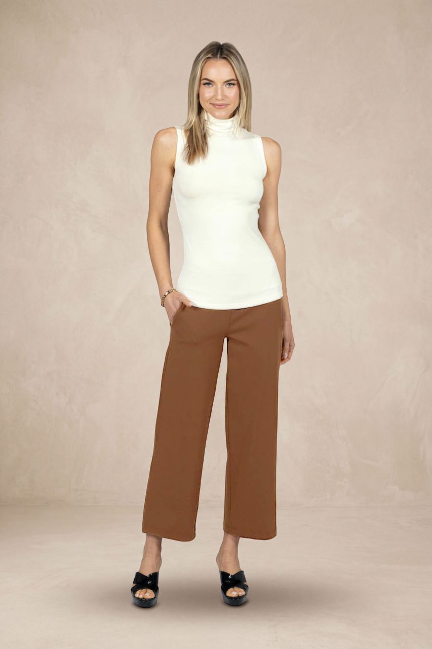 Woman wearing a white sleeveless turtleneck and brown pants on a beige background