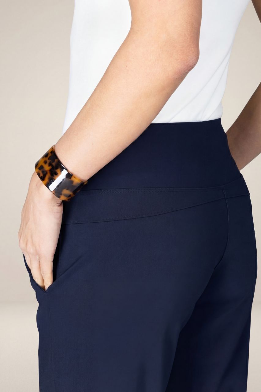 Close up view of navy blue pants worn by a person with a white top and leopard print bracelet on a neutral background