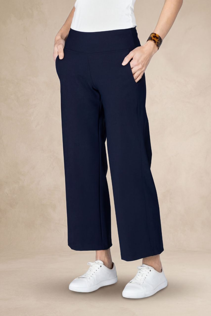 Person wearing navy ankle pants and white sneakers on a beige background