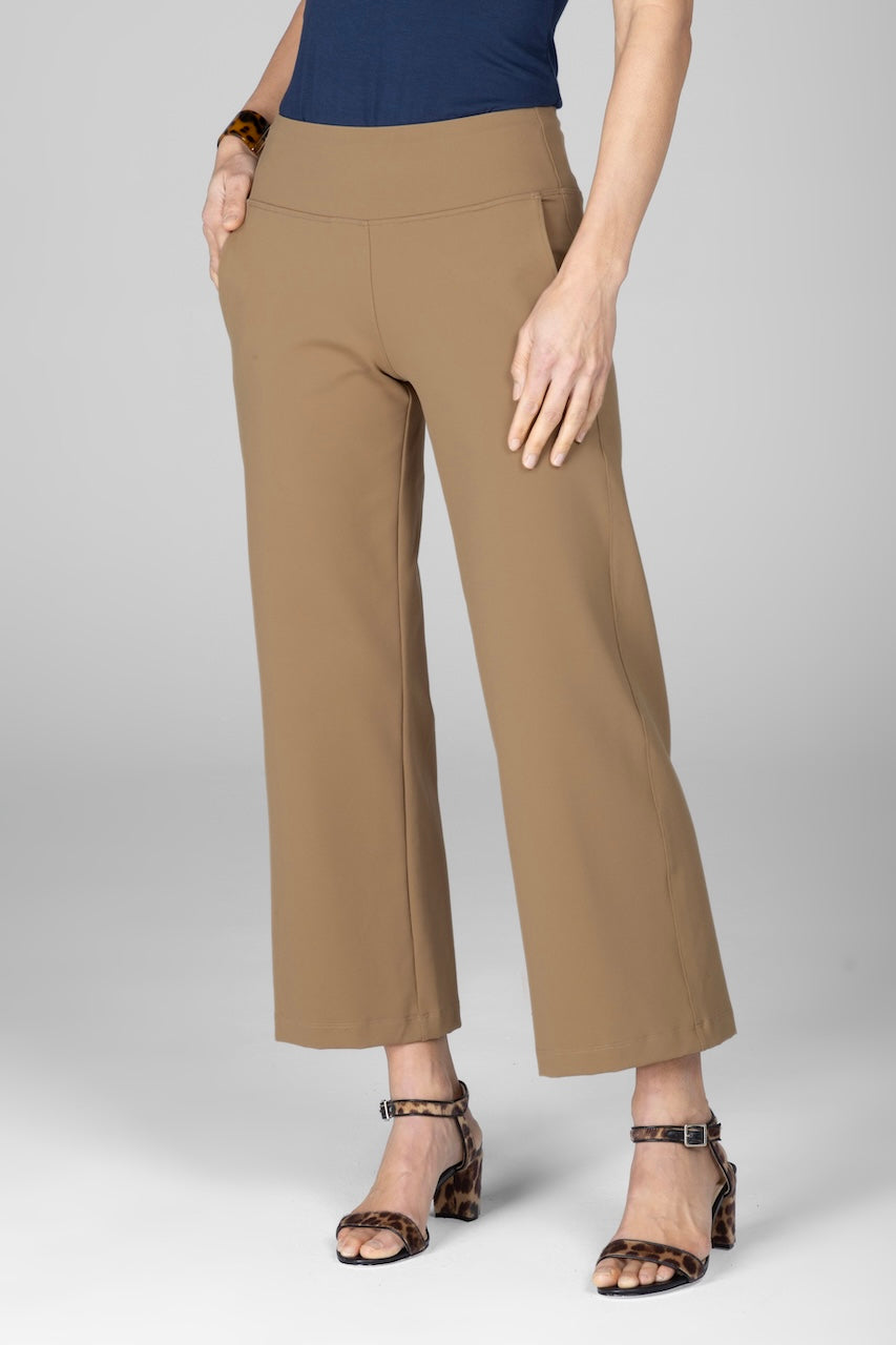 A woman wearing ankle pants in a British khaki color, paired with a navy top and brown sandals, standing against a white background.