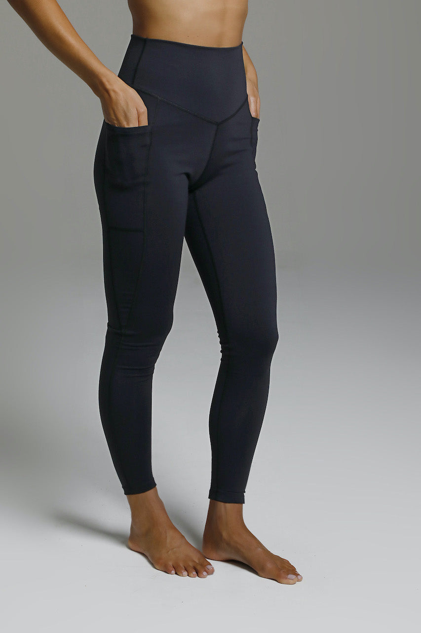 Side view of the Duchess Yoga 7/8 Legging in black, model has hands in the side pockets of the leggings