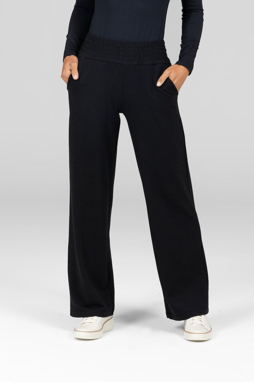 Model wearing a pair of black wide leg terry pants with a mid-waist and front pockets.