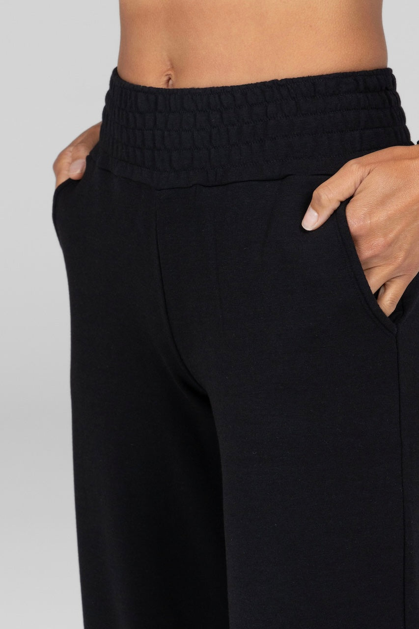 Close up photo of model wearing black mid-rise terry sweatpants with a smocked waistband